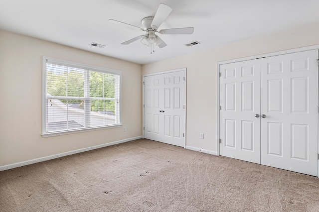 unfurnished bedroom with two closets, ceiling fan, and carpet flooring