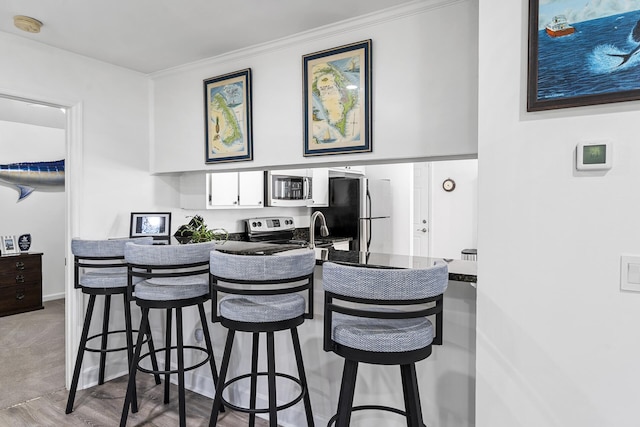 kitchen with white cabinetry, ornamental molding, stainless steel appliances, and a kitchen breakfast bar