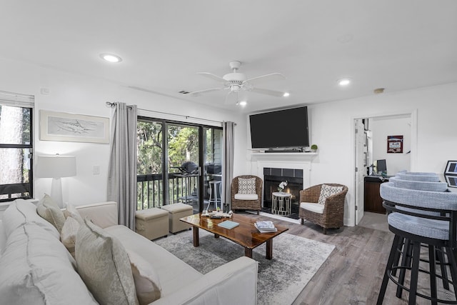 living room with ceiling fan, a tiled fireplace, and hardwood / wood-style floors