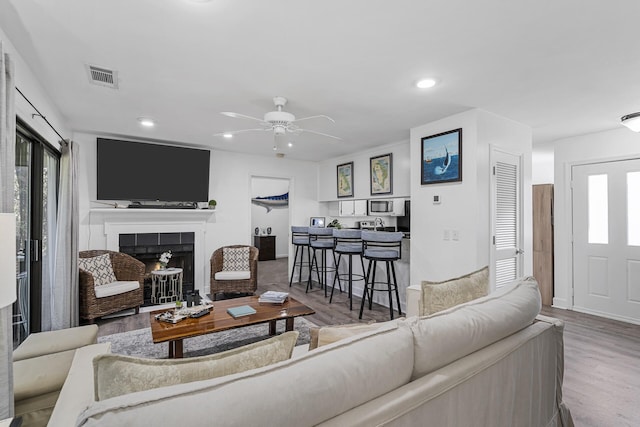 living room featuring wood-type flooring, ceiling fan, and a fireplace