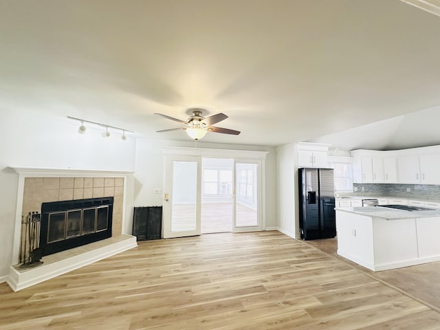 kitchen featuring light wood finished floors, open floor plan, fridge with ice dispenser, a fireplace, and white cabinets