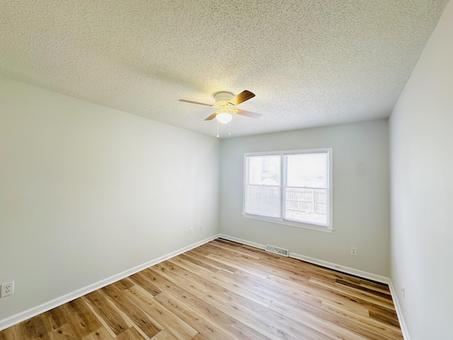 empty room featuring light wood-type flooring, visible vents, a textured ceiling, baseboards, and ceiling fan