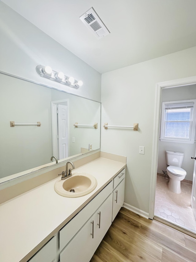 bathroom featuring visible vents, baseboards, toilet, wood finished floors, and vanity