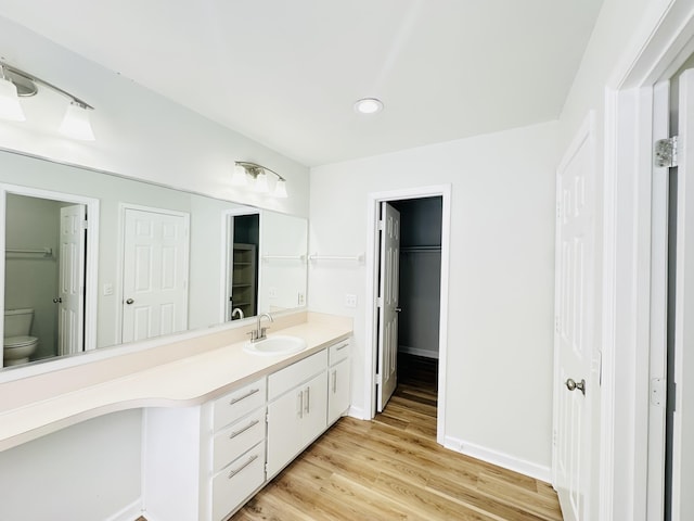 bathroom with vanity, wood finished floors, baseboards, a walk in closet, and toilet