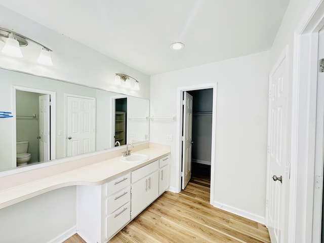 bathroom featuring baseboards, toilet, wood finished floors, and vanity