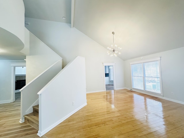 unfurnished living room featuring stairway, baseboards, high vaulted ceiling, a notable chandelier, and light wood-type flooring