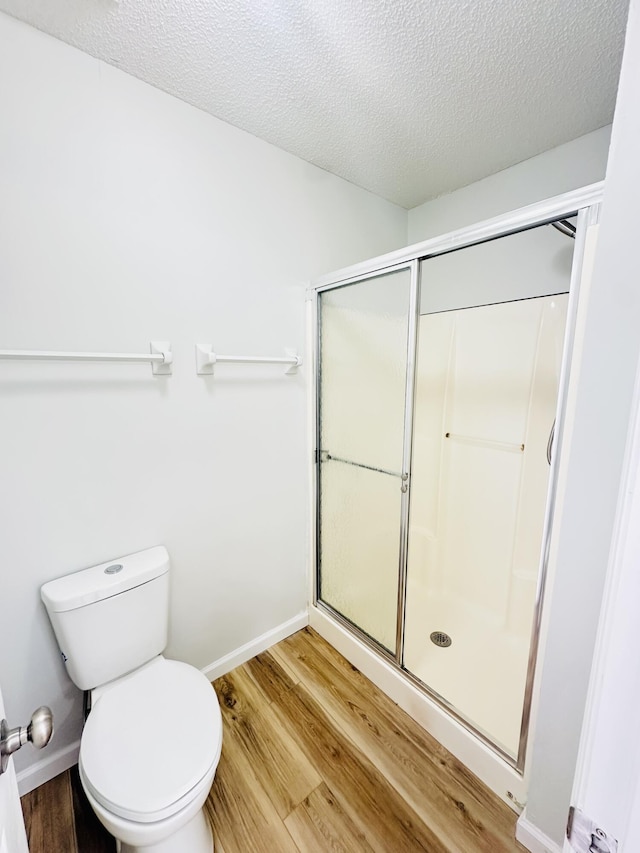 bathroom featuring toilet, wood finished floors, a shower stall, and a textured ceiling