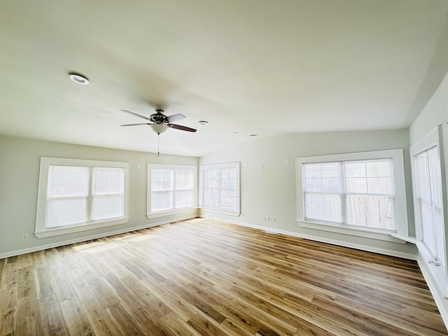 unfurnished room with plenty of natural light, a ceiling fan, baseboards, and wood finished floors