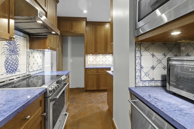 1 King Street 209 & 210, Charleston, SC 29401 - kitchen with appliances with stainless steel finishes, under cabinet range hood, brown cabinets, tasteful backsplash, and dark tile patterned floors