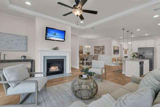 living room with crown molding, light wood-type flooring, recessed lighting, ceiling fan with notable chandelier, and visible vents