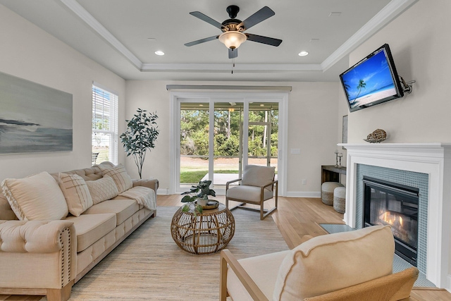 living room featuring a ceiling fan, a raised ceiling, a glass covered fireplace, light wood-style flooring, and baseboards