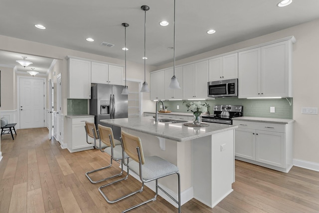 kitchen featuring light wood finished floors, white cabinetry, appliances with stainless steel finishes, a kitchen island with sink, and visible vents
