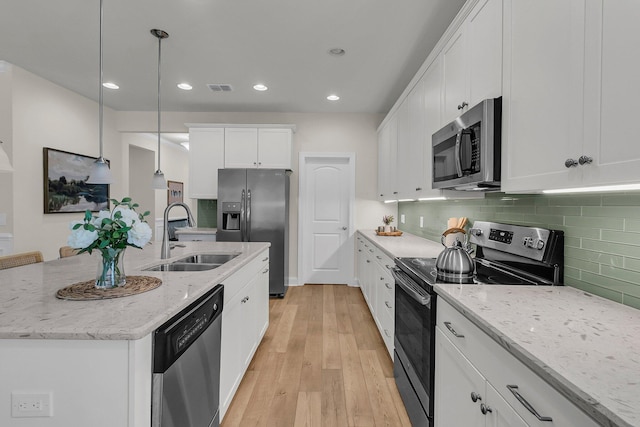 kitchen with white cabinets, light wood-style flooring, tasteful backsplash, appliances with stainless steel finishes, and a sink