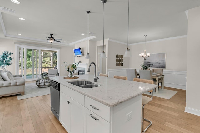 kitchen with a tray ceiling, a sink, light wood finished floors, dishwasher, and open floor plan