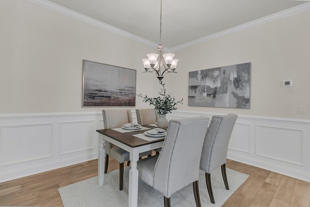 dining space featuring wainscoting, ornamental molding, a chandelier, and light wood-type flooring