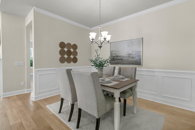 dining area with ornamental molding, a decorative wall, light wood-style floors, and a notable chandelier