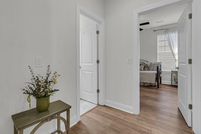 hallway with baseboards, light wood-style floors, and visible vents