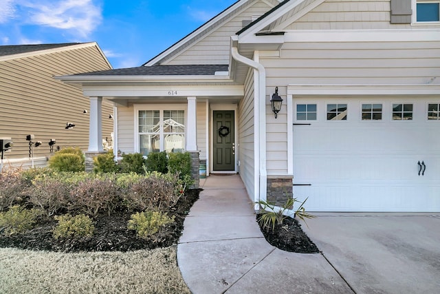 entrance to property featuring driveway, an attached garage, stone siding, and roof with shingles