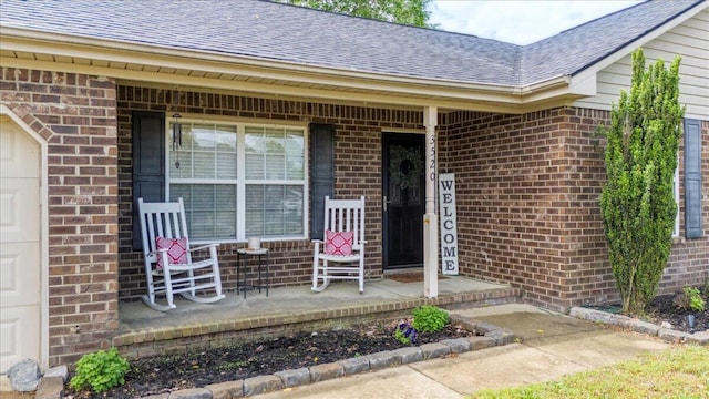 view of exterior entry featuring a porch, roof with shingles, and brick siding