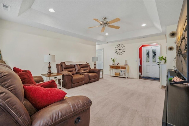 living area with visible vents, ceiling fan, a tray ceiling, arched walkways, and light carpet