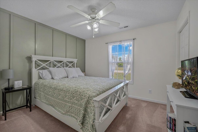 bedroom with a ceiling fan, visible vents, light carpet, baseboards, and a textured ceiling