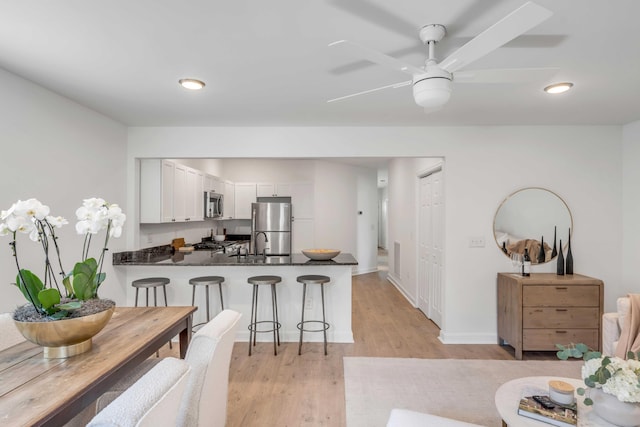 kitchen with white cabinetry, light wood-type flooring, a kitchen breakfast bar, kitchen peninsula, and stainless steel appliances