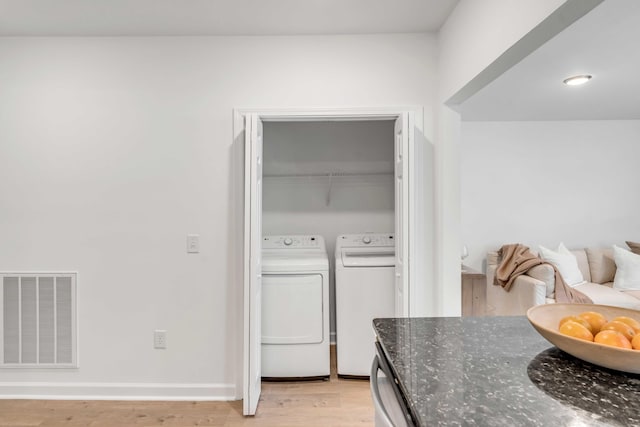 clothes washing area with washer and clothes dryer and light hardwood / wood-style floors