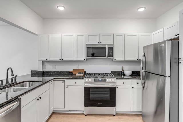 kitchen featuring white cabinetry, stainless steel appliances, sink, and dark stone countertops