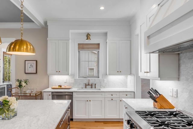 kitchen featuring appliances with stainless steel finishes, range hood, white cabinetry, and a sink