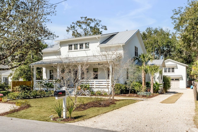 view of front facade with covered porch, an attached garage, a front yard, metal roof, and driveway