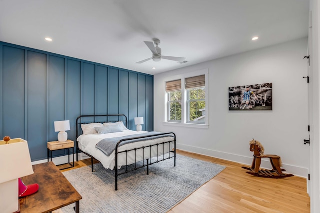 bedroom featuring recessed lighting, a decorative wall, baseboards, and wood finished floors