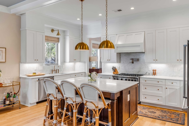 kitchen with visible vents, a kitchen island, custom range hood, stainless steel appliances, and a sink