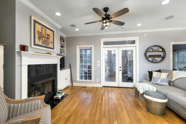 living room with ornamental molding, light wood-style flooring, a fireplace, french doors, and plenty of natural light