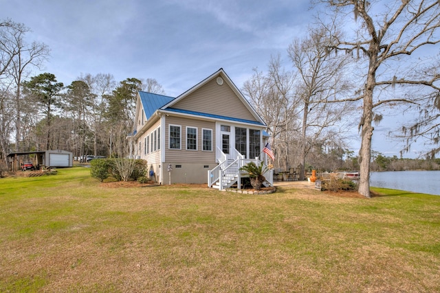 exterior space featuring a water view, a yard, an outdoor structure, a sunroom, and metal roof