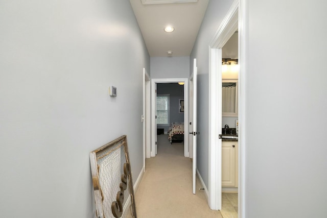 hallway with a sink, recessed lighting, baseboards, and light carpet