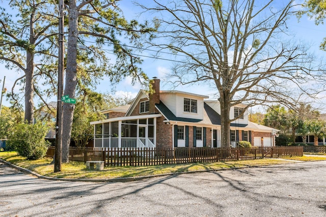 view of front facade featuring a fenced front yard, a garage, brick siding, a sunroom, and a chimney