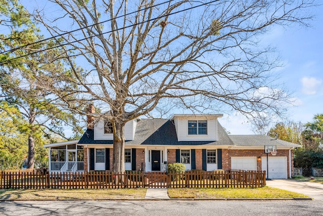 view of front of property with a fenced front yard, brick siding, an attached garage, a sunroom, and driveway