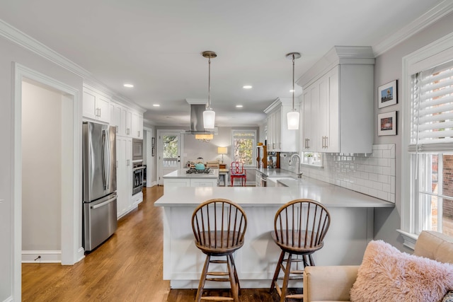 kitchen featuring stainless steel appliances, light countertops, ornamental molding, a peninsula, and wall chimney exhaust hood