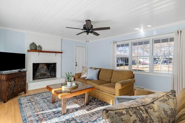 living room featuring ornamental molding, ceiling fan, a fireplace, and light hardwood / wood-style floors