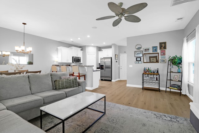 living room featuring ceiling fan with notable chandelier and light hardwood / wood-style flooring