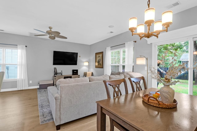 living room with light wood-type flooring, ceiling fan with notable chandelier, and plenty of natural light