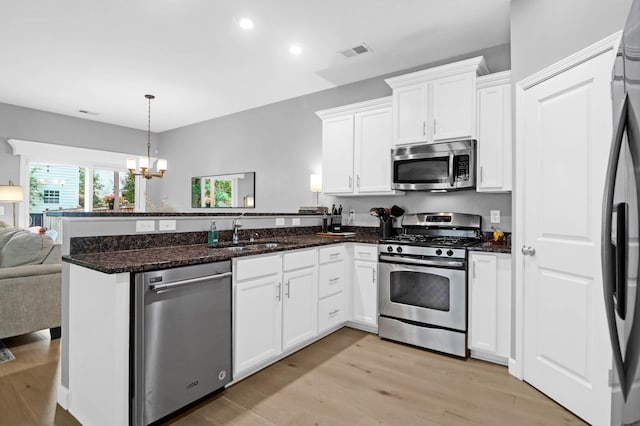 kitchen featuring sink, white cabinetry, appliances with stainless steel finishes, a notable chandelier, and light wood-type flooring