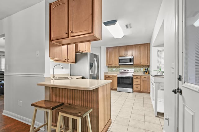 kitchen with stainless steel appliances, a sink, a peninsula, a kitchen breakfast bar, and light countertops
