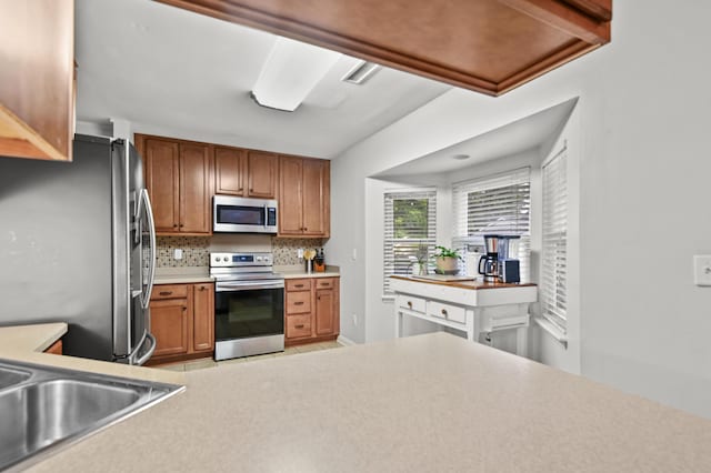 kitchen featuring stainless steel appliances, decorative backsplash, light countertops, a sink, and brown cabinets