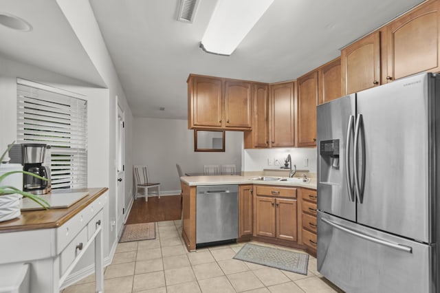 kitchen with stainless steel appliances, a sink, light tile patterned floors, baseboards, and brown cabinetry