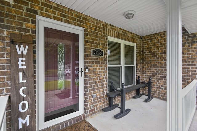 view of exterior entry featuring brick siding and a porch