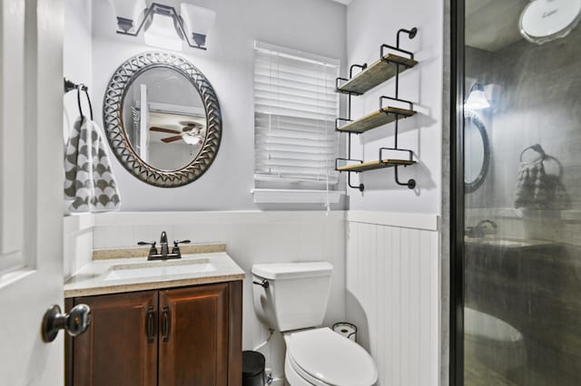 bathroom with a wainscoted wall, a stall shower, vanity, a ceiling fan, and toilet