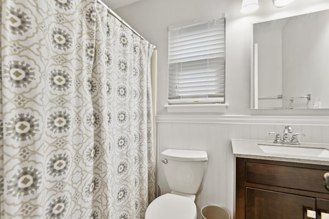 full bathroom featuring wainscoting, toilet, vanity, and curtained shower