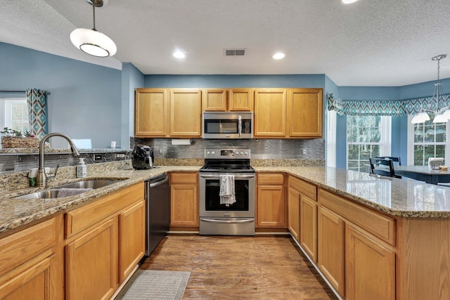 kitchen with pendant lighting, sink, backsplash, stainless steel appliances, and kitchen peninsula