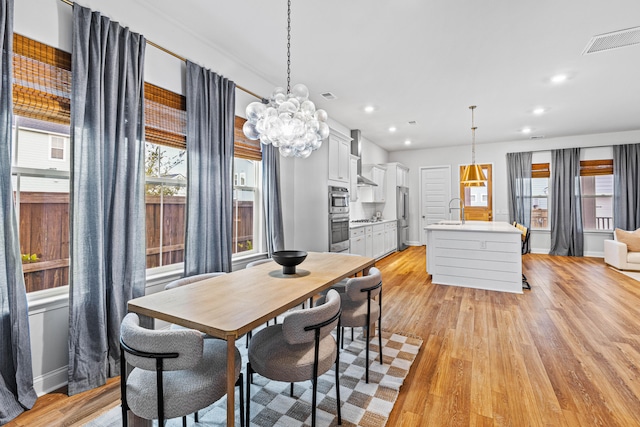 dining area with light hardwood / wood-style flooring, a notable chandelier, and sink